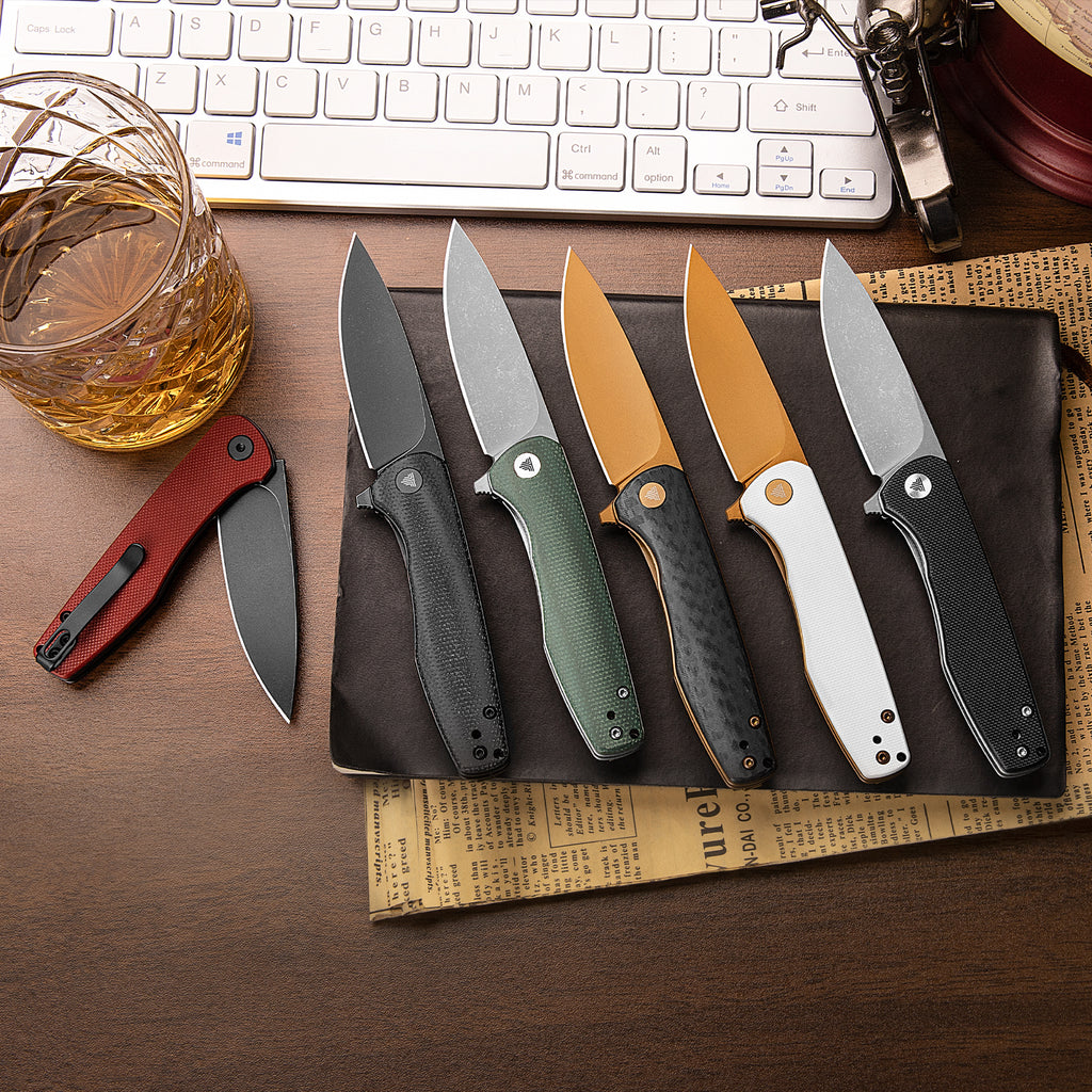 Set of tactical knives with various handle colors and drop point blades on wooden desk