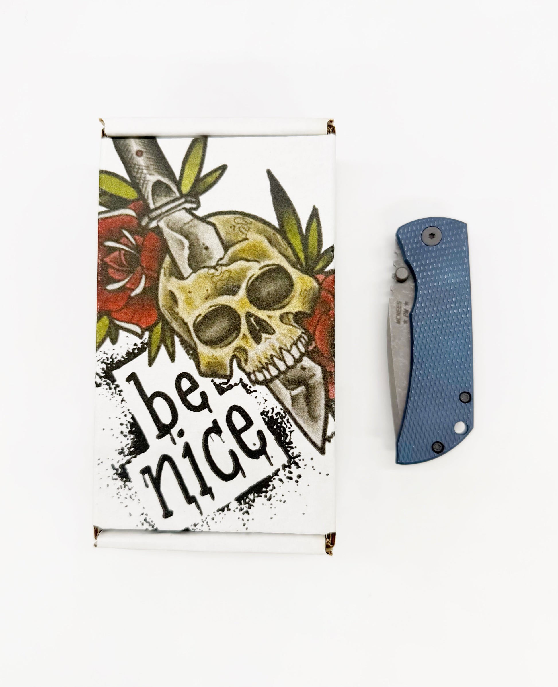 Blue titanium folding knife with textured handle and blade next to skull sticker