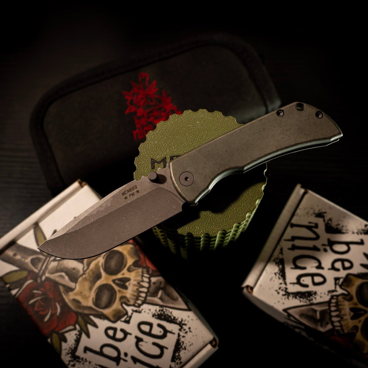 McNees Knives PM Mac 2 Gen 2 with 3-inch MagnaCut blade, green/bronze titanium handles, on skull-themed packaging