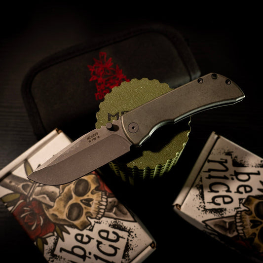 McNees Knives PM Mac 2 Gen 2 with 3-inch MagnaCut blade, green/bronze titanium handles, on skull-themed packaging