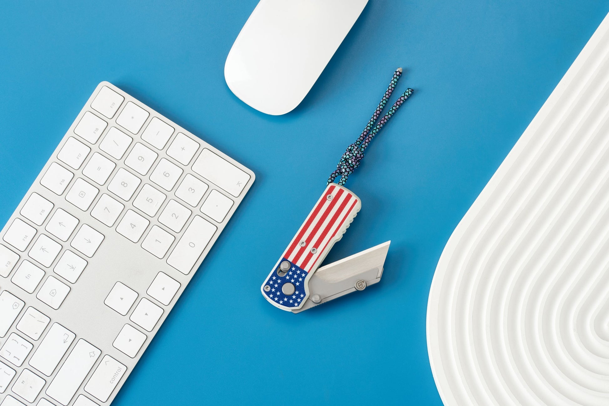 Oknife U1 Stars & Stripes folding utility knife with blade deployed on a desk beside a keyboard, showing the USA flag G10 handle and lanyard