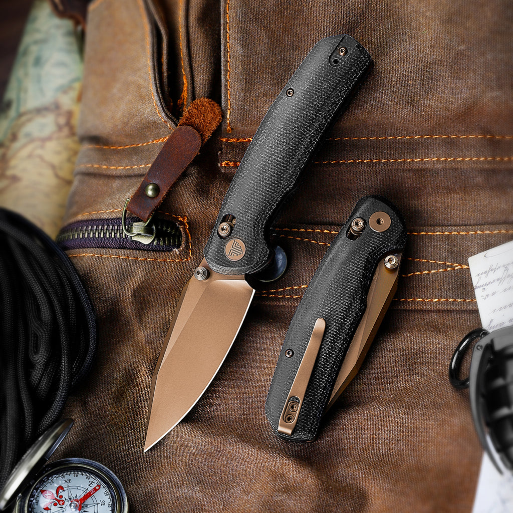 Black tactical folding knife with textured handle on rugged outdoor gear