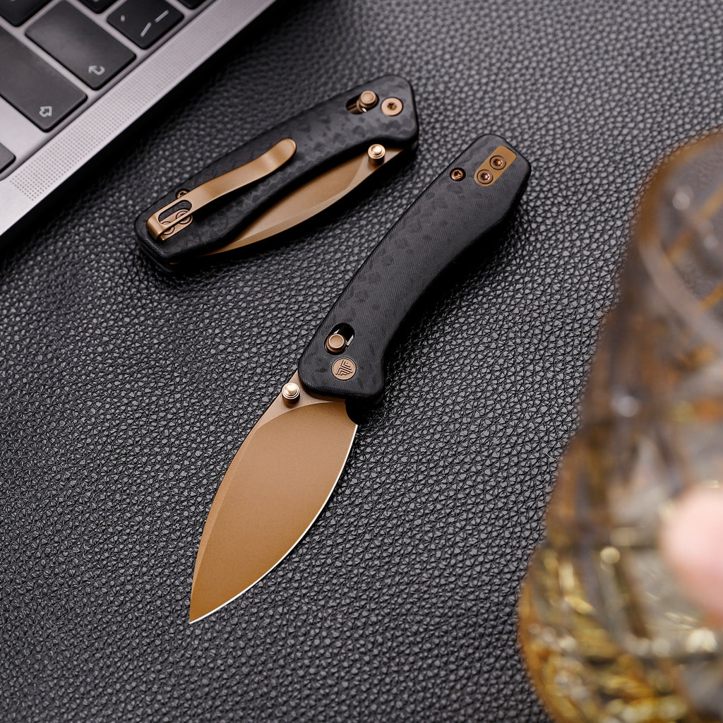 Black and gold folding knife with drop point blade and carbon fiber handle